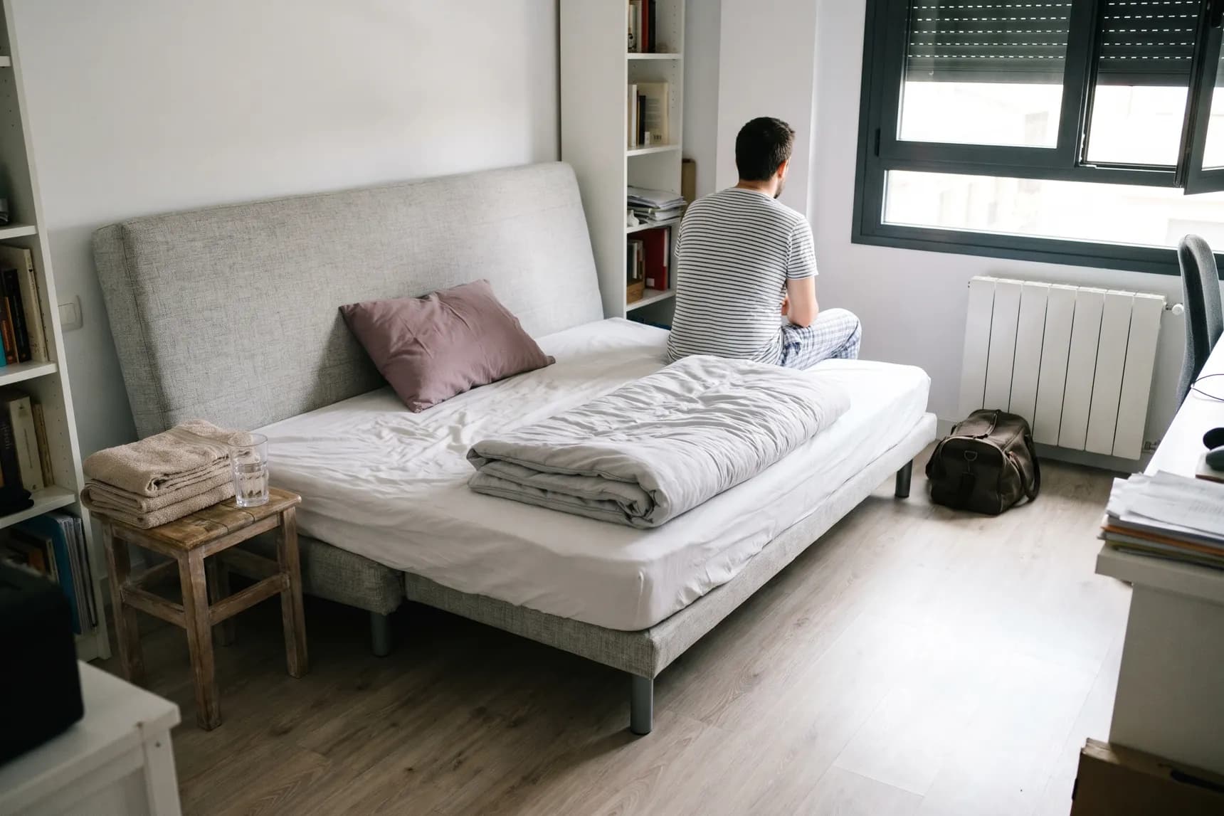 Sofá cama clic clac abierto en un salón-despacho, con toallas dobladas y una bolsa de viaje al lado (imagen generada con IA)